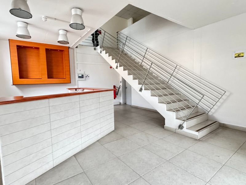 A bright, modern industrial entry foyer featuring a tiled reception desk, a prominent staircase with metal railings, and clean, neutral finishes.
