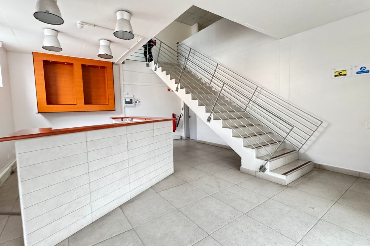 A bright, modern industrial entry foyer featuring a tiled reception desk, a prominent staircase with metal railings, and clean, neutral finishes.
