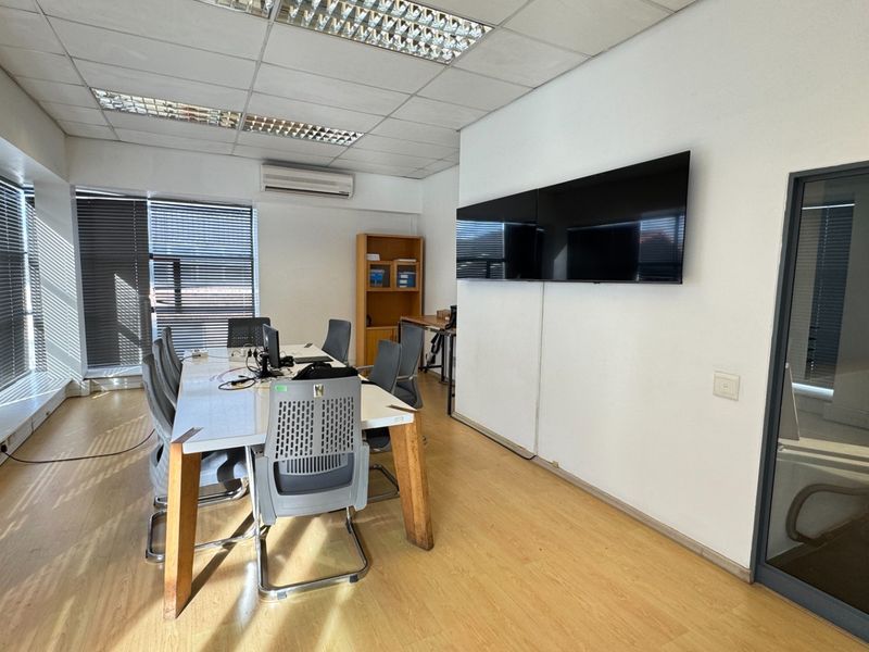 A functional office space featuring laminate flooring, suspended ceilings with recessed lighting, split-system air conditioning, and large windows with venetian blinds.