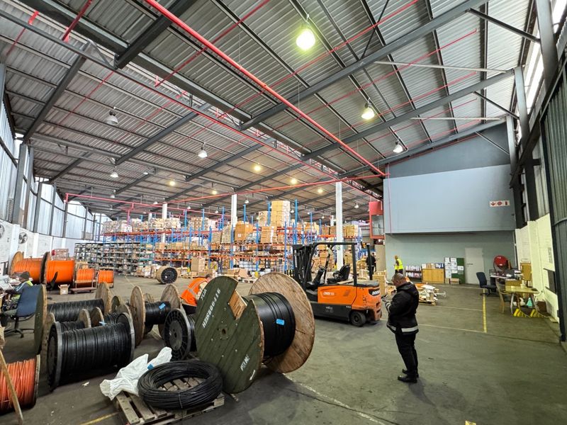 Spacious industrial warehouse featuring high ceilings with exposed steel trusses, fire sprinkler system, and durable concrete flooring, suitable for storage or manufacturing operations.