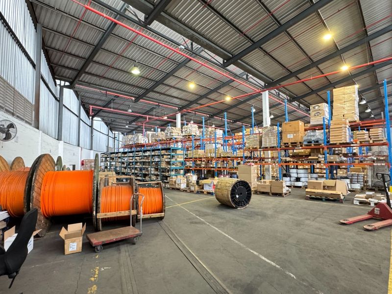 Spacious industrial warehouse featuring high ceilings with exposed steel trusses, fire sprinkler system, high-bay lighting, and extensive heavy-duty racking for storage.