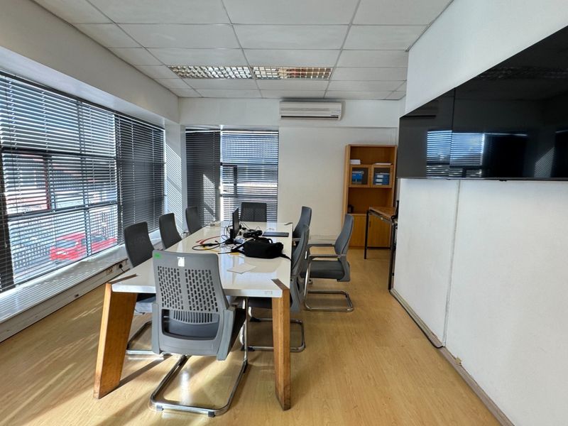 A functional office space featuring laminate flooring, suspended ceilings, wall-mounted air conditioning, and large windows with venetian blinds.