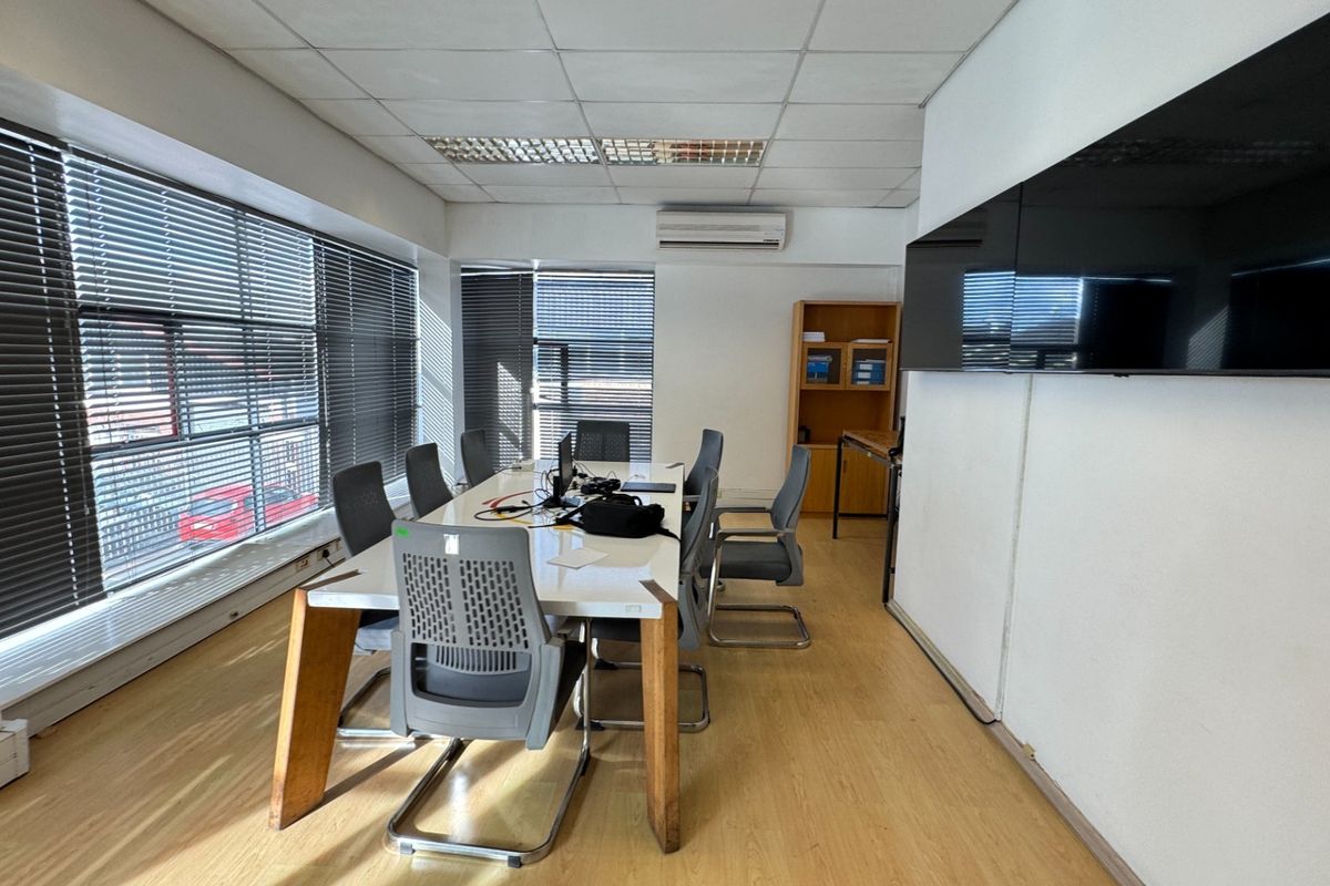 A functional office space featuring laminate flooring, suspended ceilings, wall-mounted air conditioning, and large windows with venetian blinds.