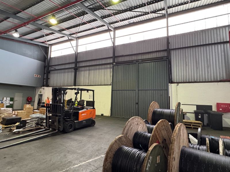 Spacious industrial warehouse featuring high ceilings with exposed steel trusses, fire safety systems, and a large sliding access door.