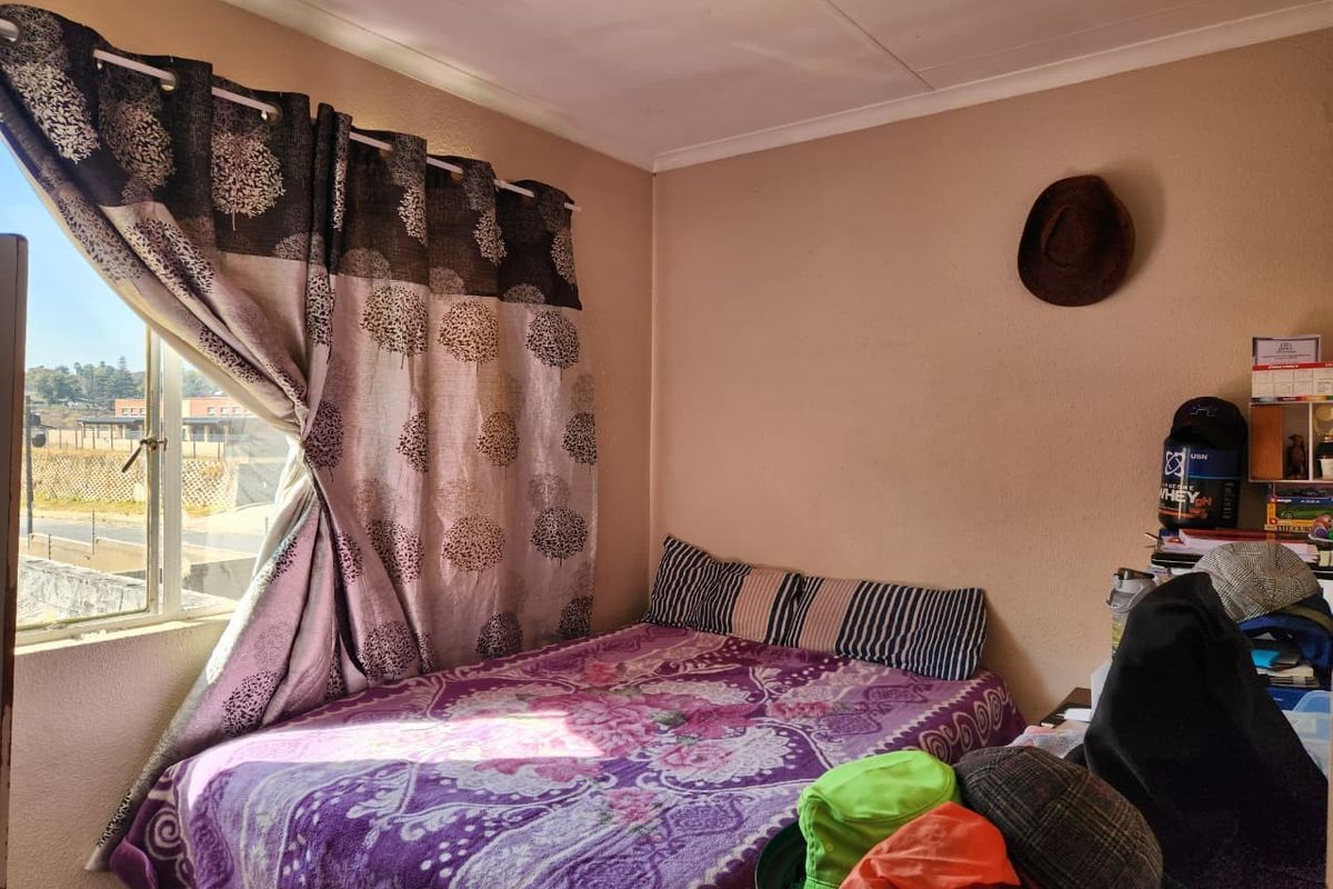 A standard bedroom featuring a window with aluminium frames, providing natural light and a view of the surrounding area.