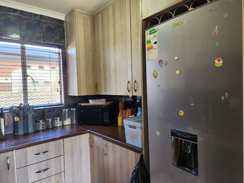 A functional kitchen featuring wood-look laminate cabinetry, dark countertops, and a tiled backsplash, providing practical storage and workspace.