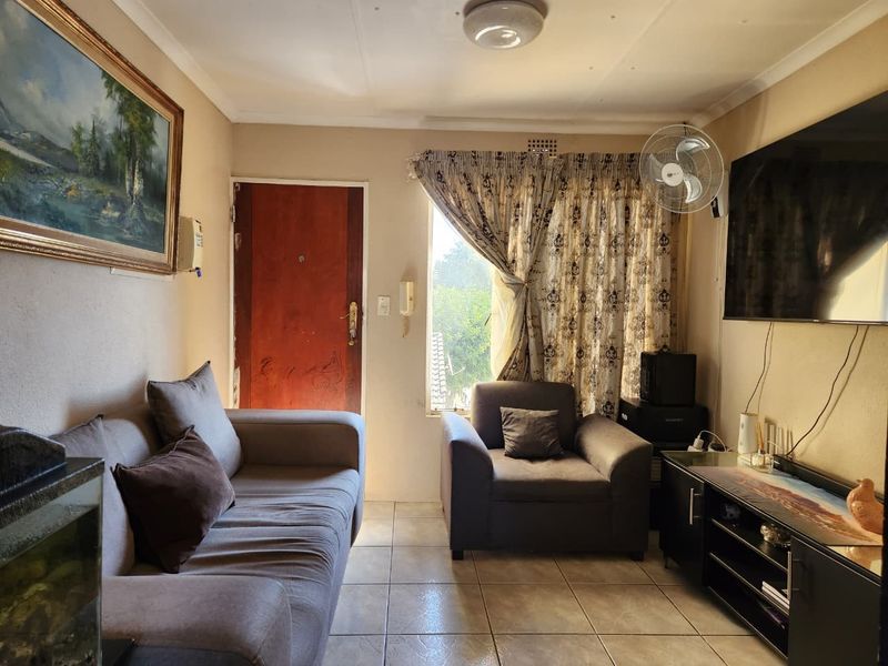A compact living room featuring tiled flooring, an intercom system, and a wall-mounted fan, providing a functional and cozy living space.