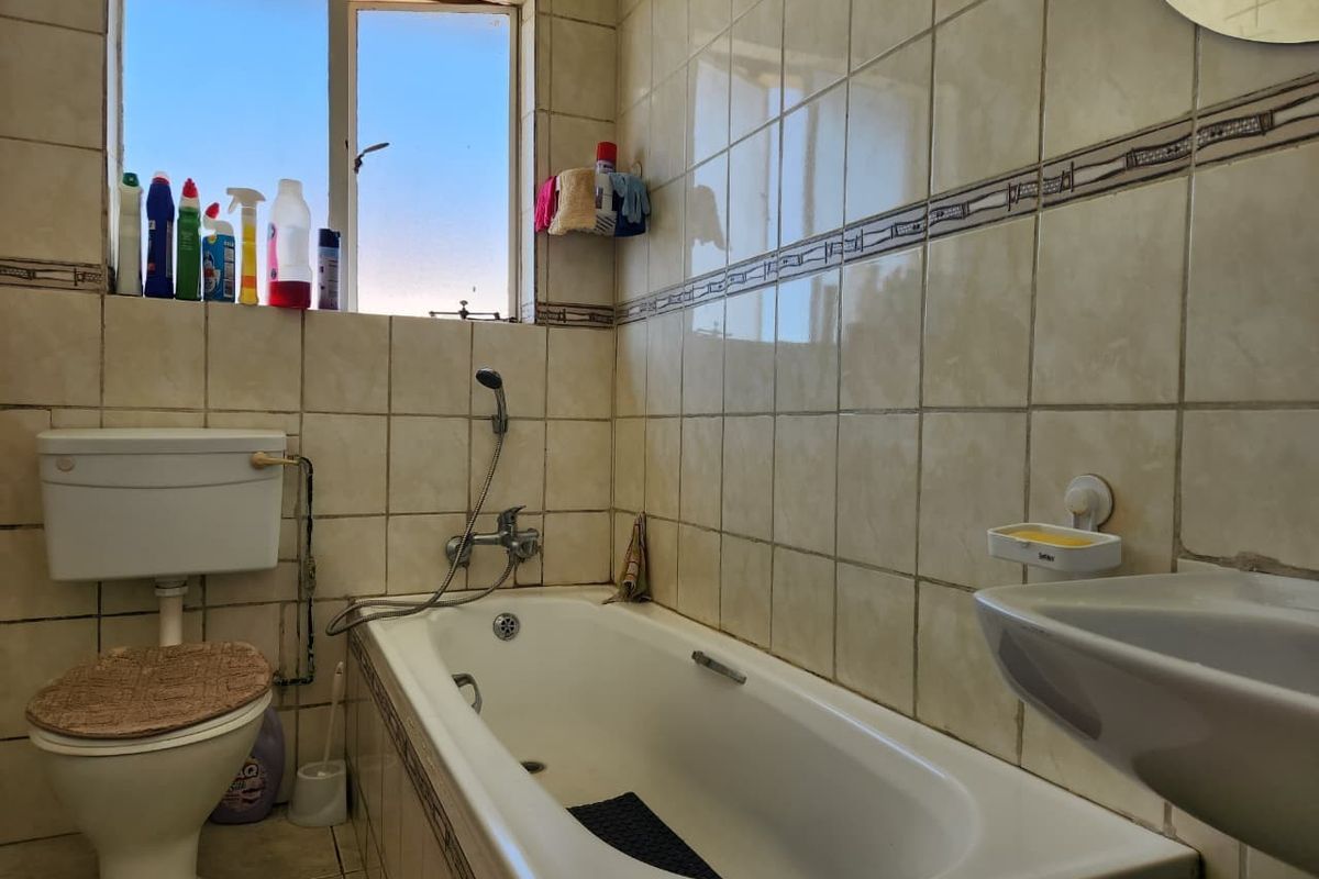 A functional bathroom featuring a bathtub with a handheld shower mixer, a standard toilet, and a washbasin with tiled wall finishes.