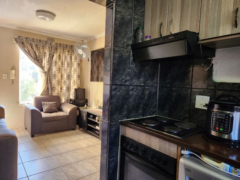 Open plan living area featuring a compact kitchen with built-in cabinetry, electric stove, and extractor fan, flowing into a tiled lounge space.