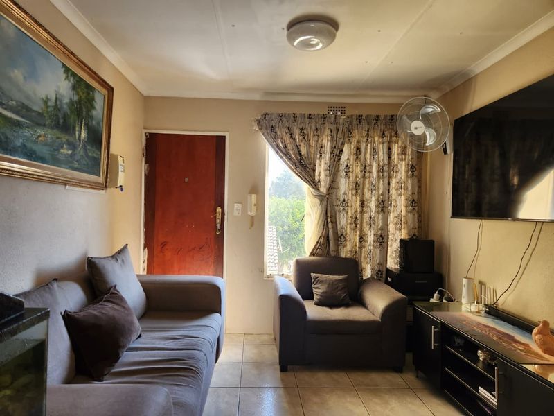 A compact living room featuring tiled flooring, a wall-mounted intercom, and a ceiling light fixture, providing a functional space for relaxation.
