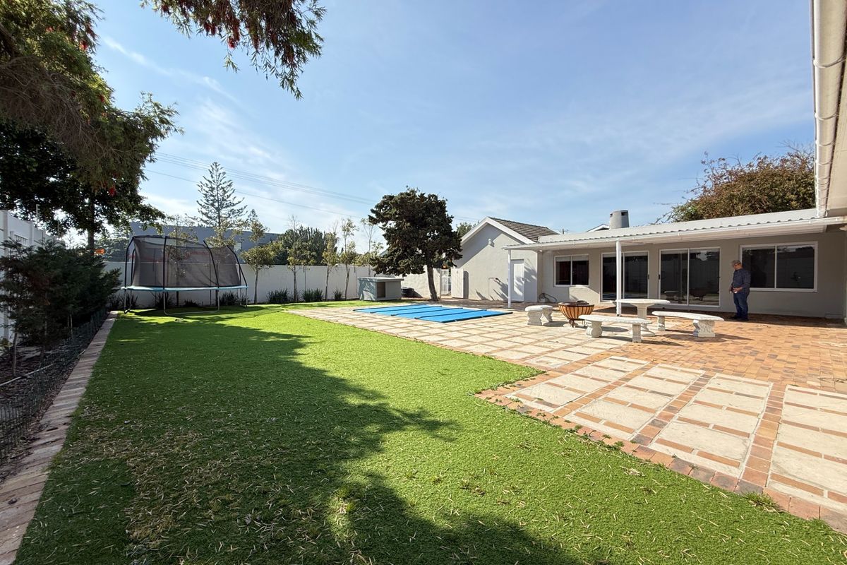 Spacious rear garden featuring a paved patio area, covered entertainment space, swimming pool, and well-maintained artificial lawn enclosed by a boundary wall.