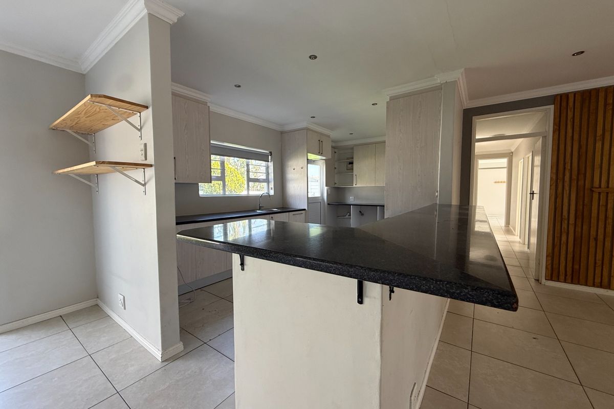 Open-plan kitchen featuring a breakfast bar, stone countertops, and light-toned cabinetry, with direct access to the hallway and living area.