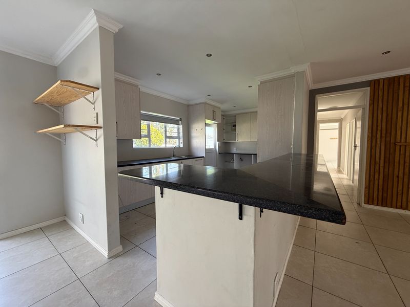 Open-plan kitchen featuring a breakfast bar, stone countertops, and light-toned cabinetry, with direct access to the hallway and living area.