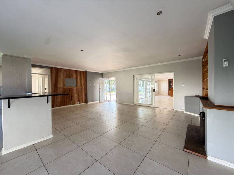 Spacious open-plan living area featuring large format floor tiles, a timber slat feature wall, built-in fireplace, and seamless access to the outdoor patio.