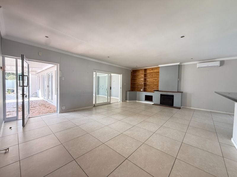Spacious living area featuring large floor tiles, a built-in fireplace with wooden shelving, and direct access to an outdoor patio through sliding glass doors.