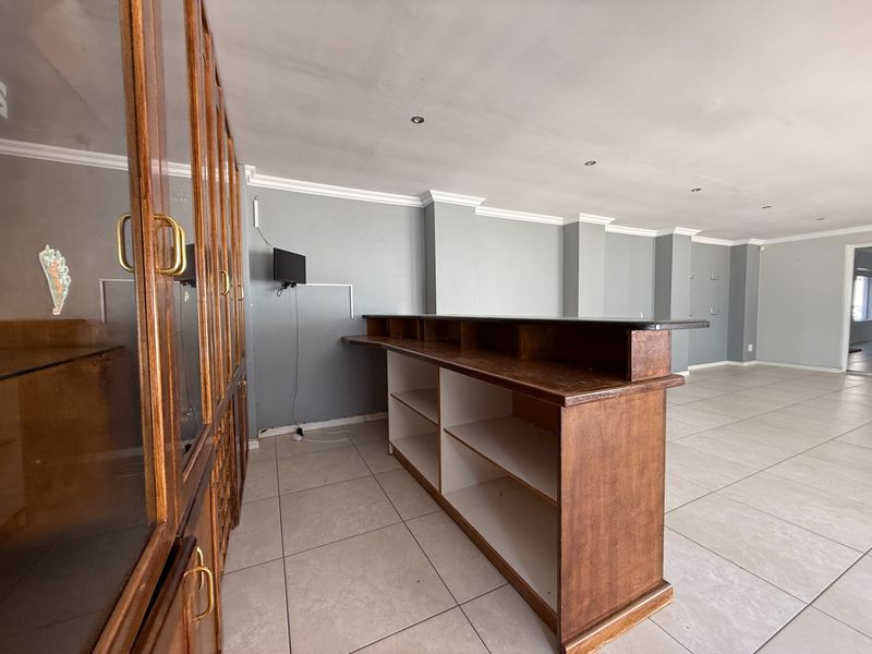 A dedicated bar area featuring a built-in wooden counter, extensive cabinetry, tiled flooring, and recessed lighting, offering potential for a modern entertainment space.