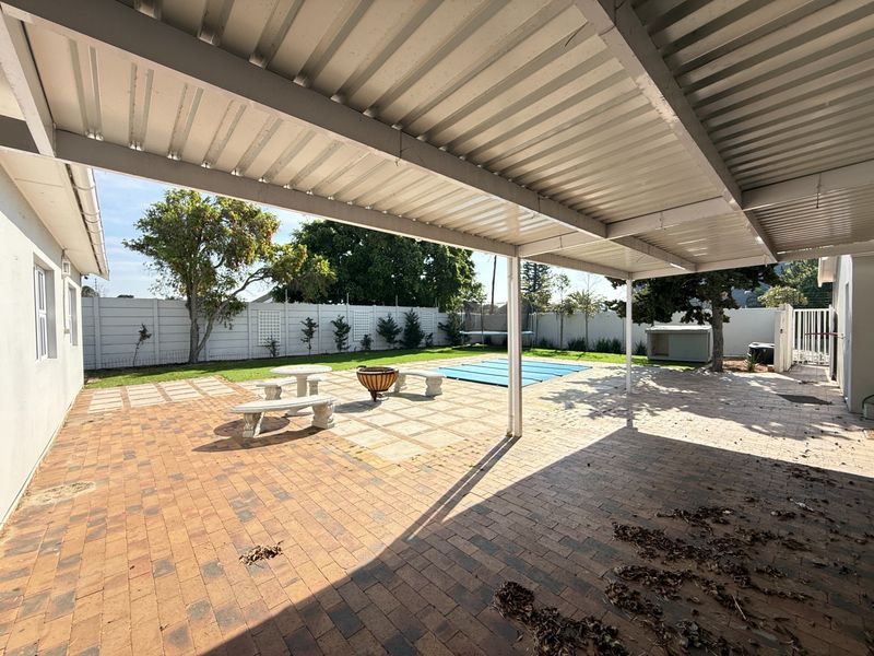 Spacious covered patio area featuring paved flooring, overlooking a private garden and swimming pool with a secure boundary wall.