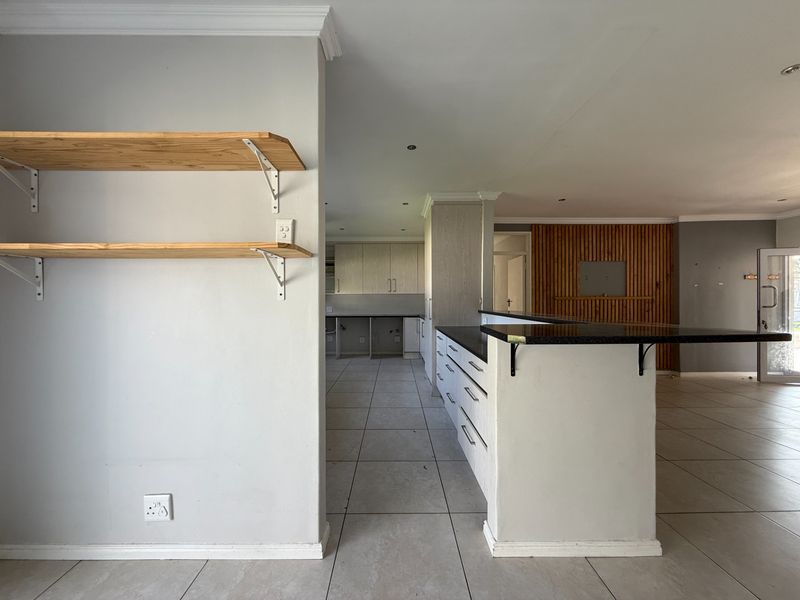 Open-plan living and kitchen area featuring tiled floors, a breakfast bar with granite countertops, and decorative timber wall paneling.