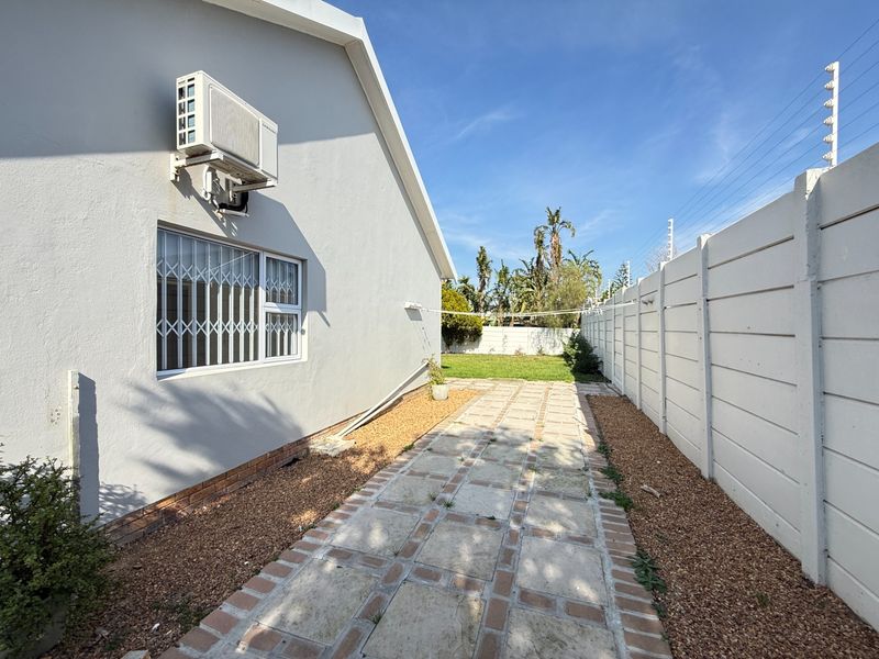 A side exterior view of the property featuring a paved walkway, gravel landscaping, security bars on the window, and a precast concrete boundary wall.