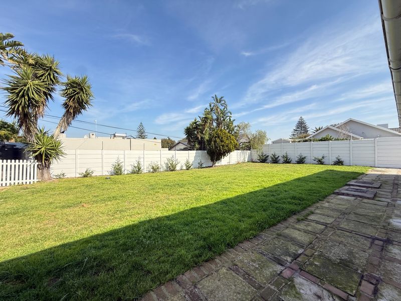 A spacious rear garden featuring a well-maintained lawn, a paved patio area, and secure precast concrete boundary walling.