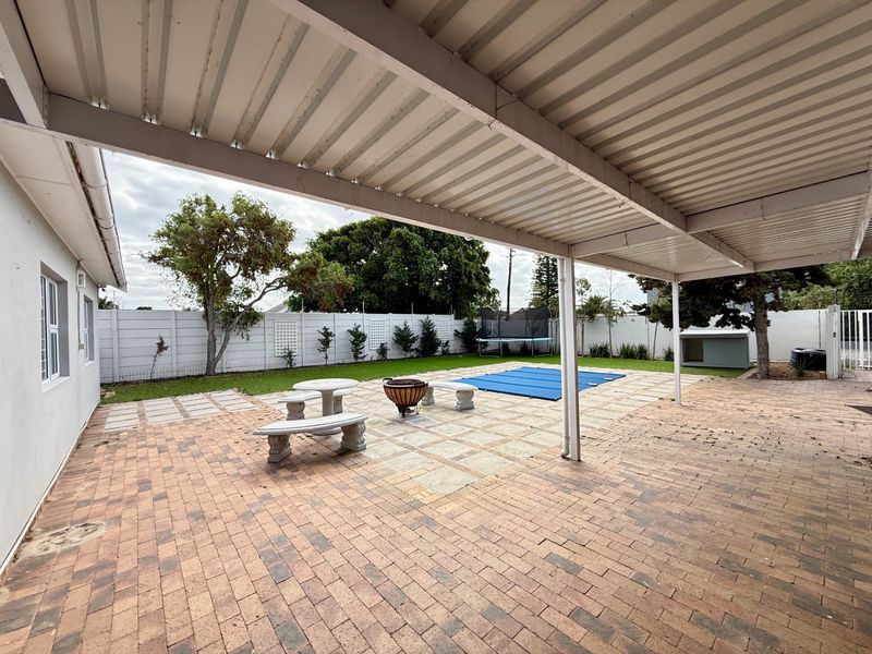 Spacious covered patio area featuring paved flooring, overlooking a private garden with a swimming pool and secure boundary wall.