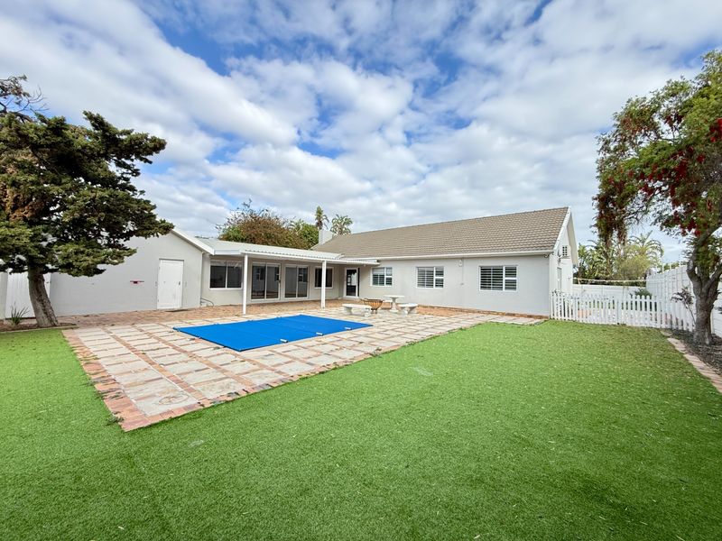 Rear exterior view featuring a swimming pool with cover, a covered patio area, and a well-maintained artificial lawn in the backyard.