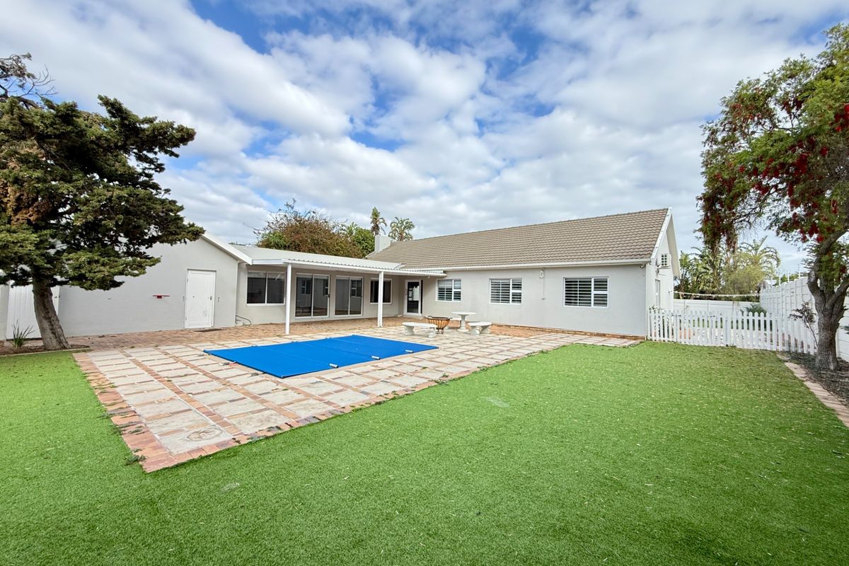 Rear exterior view featuring a swimming pool with cover, a covered patio area, and a well-maintained artificial lawn in the backyard.