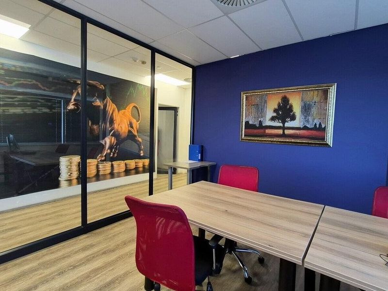 A modern commercial office space featuring a glass partition wall, suspended ceiling, and durable laminate flooring, suitable for professional meetings or workspace.