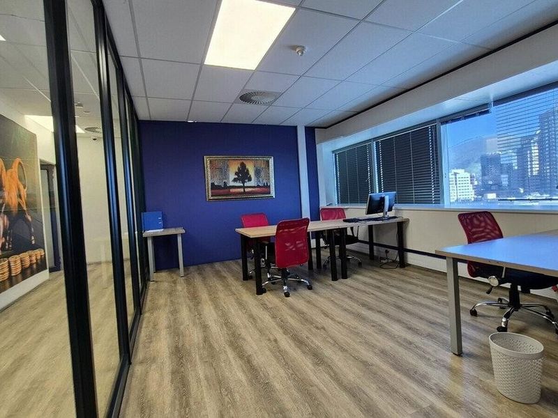 A modern commercial office space featuring laminate flooring, glass partitioning, suspended ceilings with recessed lighting, and large windows providing natural light and city views.