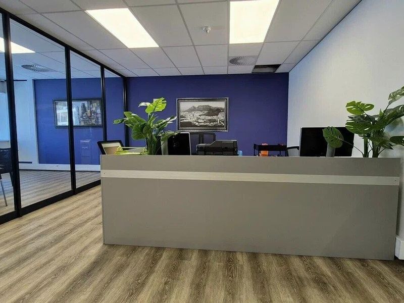 Modern commercial office space featuring a built-in reception desk, glass partition walls, laminate flooring, and a clean suspended ceiling with recessed lighting.
