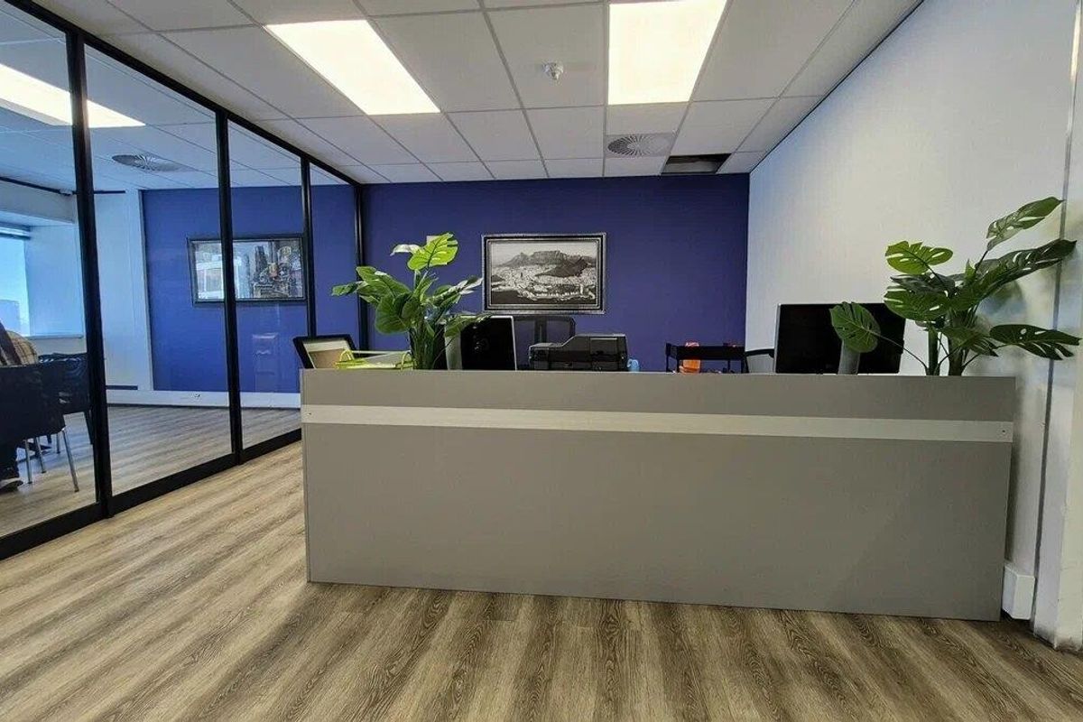 Modern commercial office space featuring a built-in reception desk, glass partition walls, laminate flooring, and a clean suspended ceiling with recessed lighting.