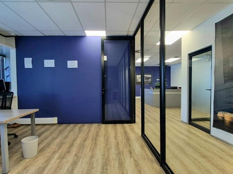 Modern commercial office space featuring glass partition walls, wood-look laminate flooring, and a suspended ceiling with recessed lighting.