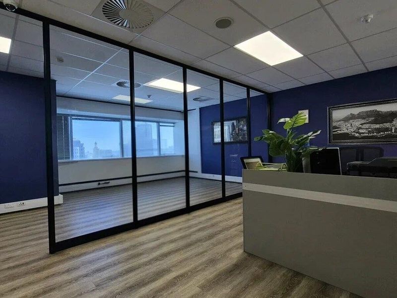 Modern commercial office space featuring a glass-partitioned private office, laminate flooring, and recessed ceiling lighting in a professional corporate environment.
