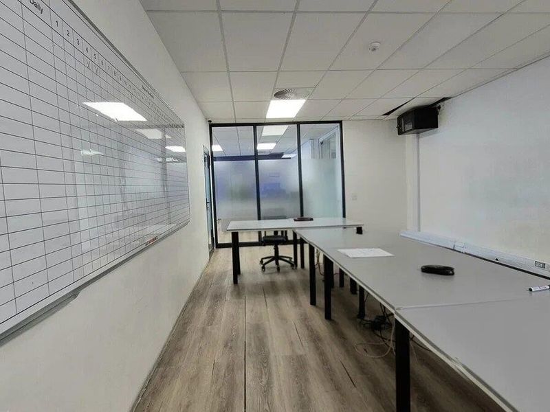 A functional office space featuring laminate flooring, a suspended ceiling with recessed lighting, and a glass partition wall for a professional work environment.