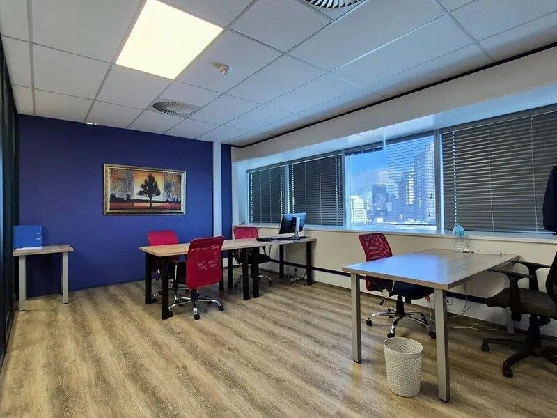 A functional commercial office space featuring laminate flooring, a suspended ceiling with recessed lighting, and large windows with venetian blinds.