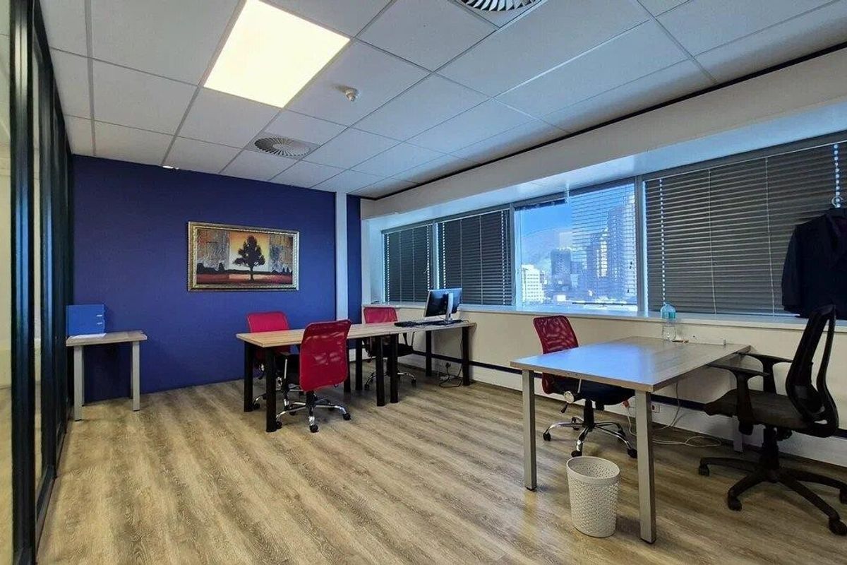A functional commercial office space featuring laminate flooring, a suspended ceiling with recessed lighting, and large windows with venetian blinds.