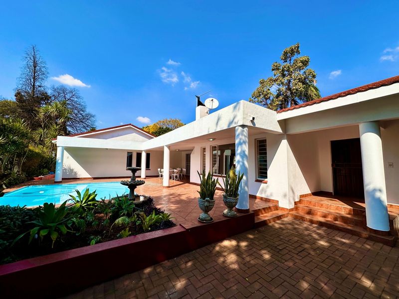 Spacious outdoor entertainment area featuring a swimming pool, covered patio with terracotta paving, and a central fountain set within a landscaped garden.