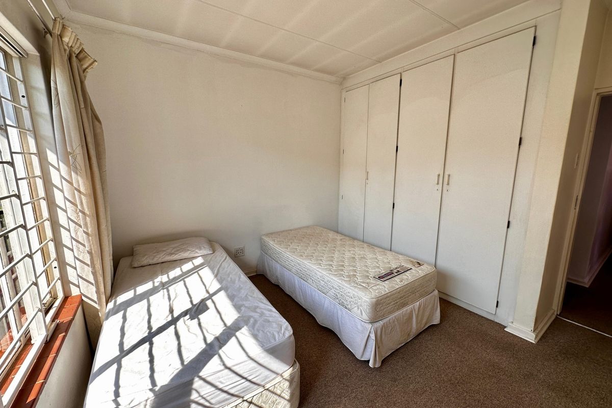 A bedroom featuring built-in cupboards, carpeted flooring, and security bars on the window, offering a functional space in need of cosmetic updates.