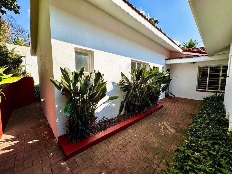 A well-maintained rear exterior area featuring brick paving, a raised garden bed, and white rendered walls under a tiled roof.