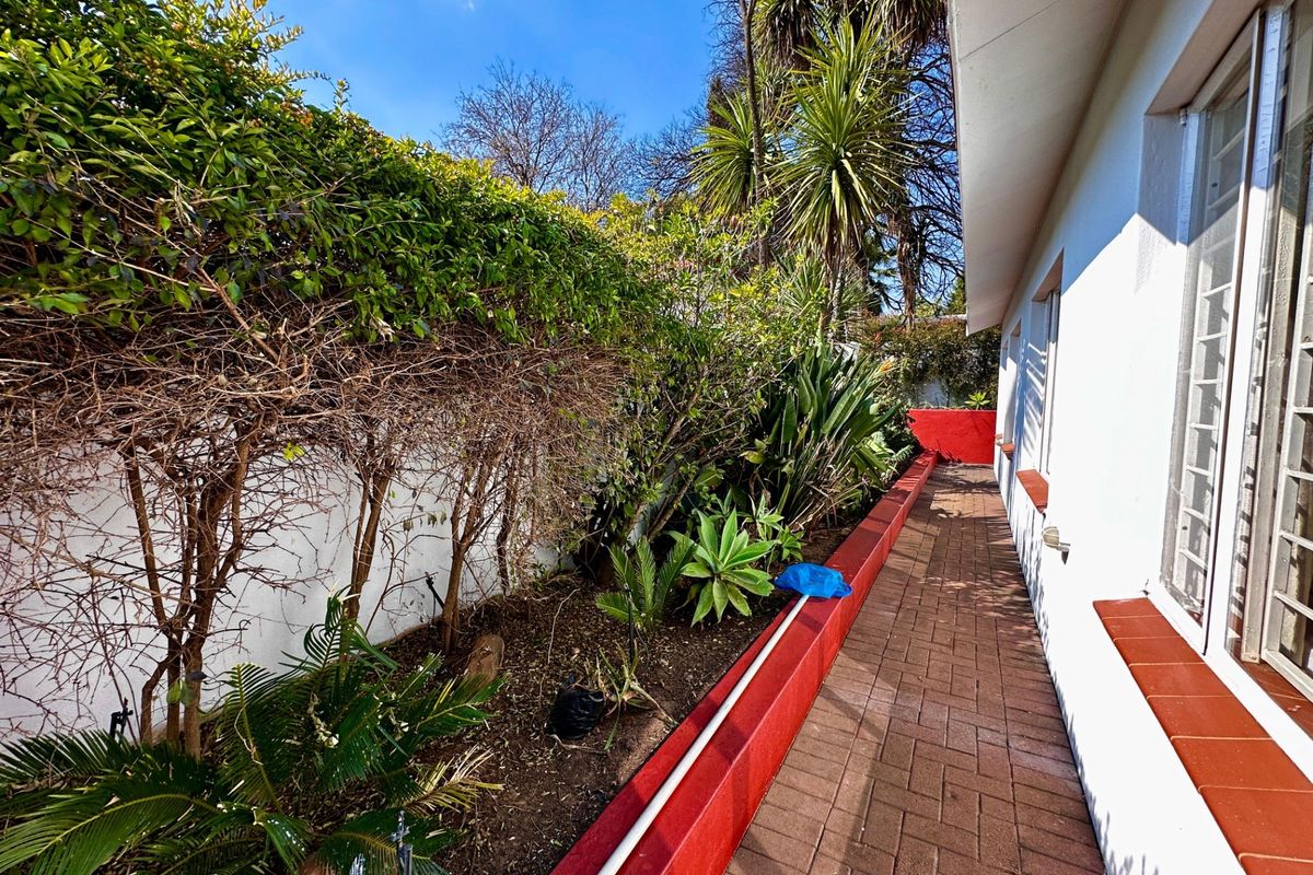 A side exterior view featuring a paved walkway alongside a landscaped garden bed with a painted retaining wall.