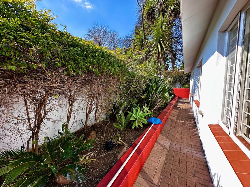 A side exterior view featuring a paved walkway alongside a landscaped garden bed with a painted retaining wall.