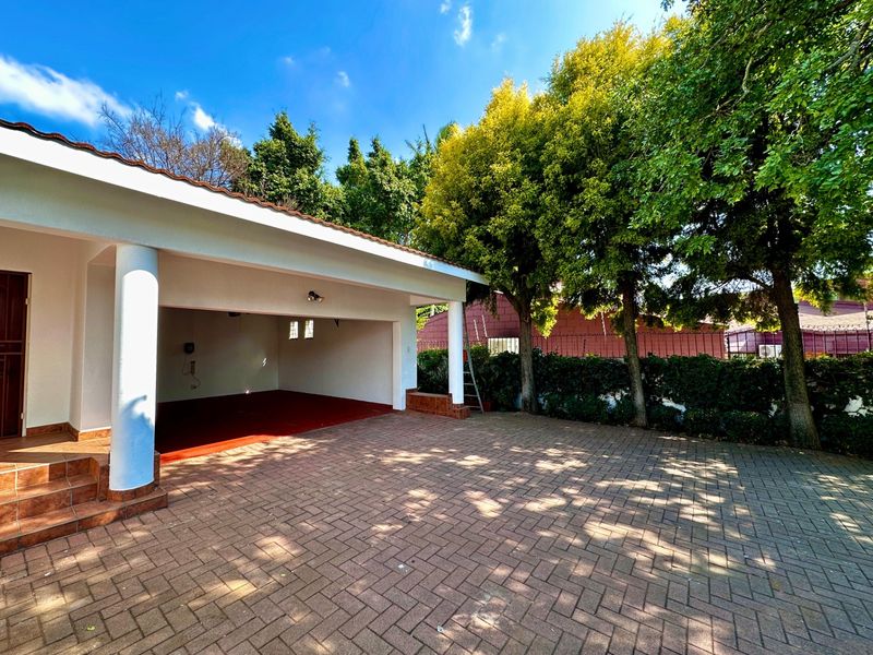A spacious open-plan carport with paved driveway access, featuring tiled flooring and sturdy structural columns, providing convenient covered parking.