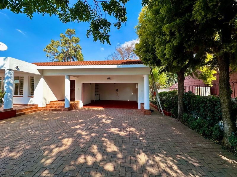 A well-maintained open-plan garage with a paved driveway, featuring structural columns and a classic terracotta tiled roof.