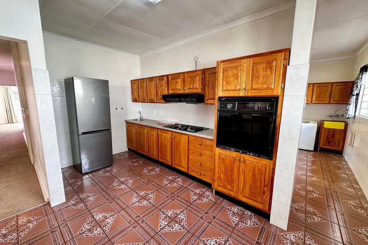 A functional kitchen featuring traditional wooden cabinetry, built-in oven, cooktop, extractor fan, and patterned tiled flooring.
