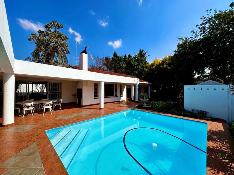 Spacious outdoor entertainment area featuring a swimming pool, covered patio with built-in braai, and tiled flooring, ideal for relaxed outdoor living.