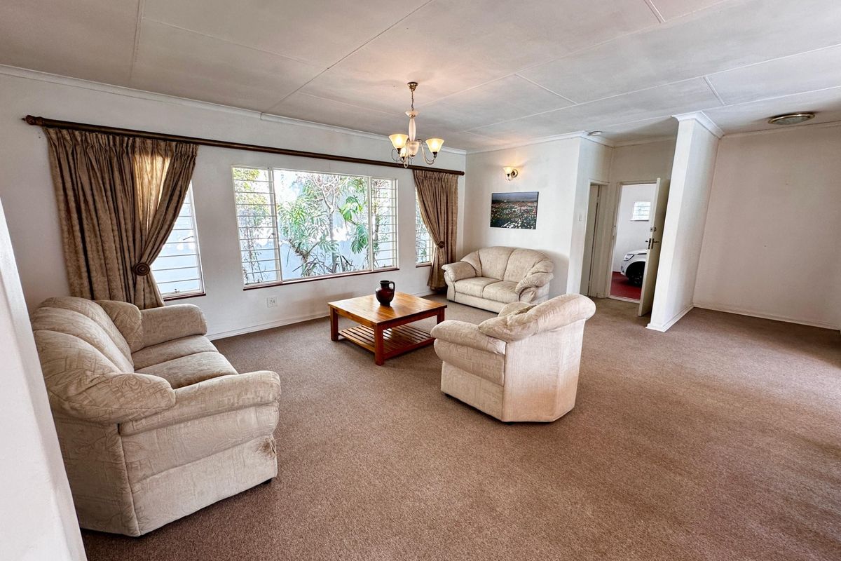 Spacious living room featuring carpeted flooring, large windows with security bars, and classic ceiling detailing, offering a comfortable and functional layout.