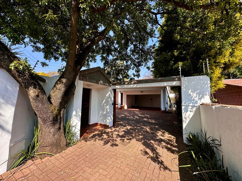 Front entrance view featuring a paved driveway, covered carport, and secure boundary wall with electric fencing.