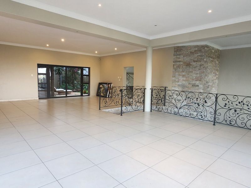 Spacious open-plan living area featuring large format floor tiles, a decorative wrought iron balustrade, and a striking stone-clad feature wall.
