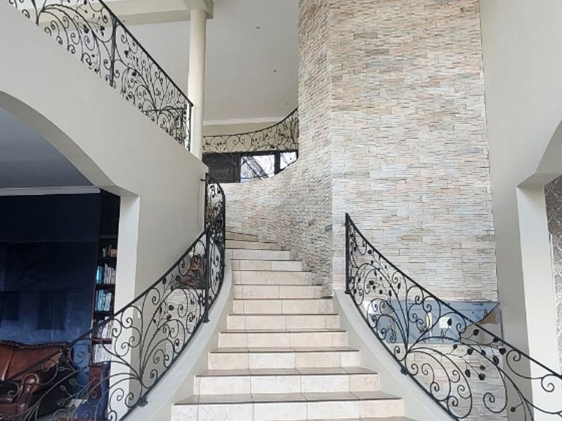 Grand entrance foyer featuring a sweeping staircase with ornate wrought iron balustrades and a striking stone feature wall.
