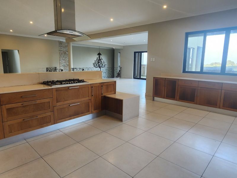 Spacious kitchen featuring extensive wooden cabinetry, stone countertops, a gas hob with extractor, and large windows providing ample natural light.